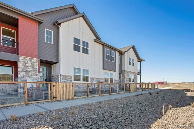 rear view of property with board and batten siding, central air condition unit, fence, and stone siding
