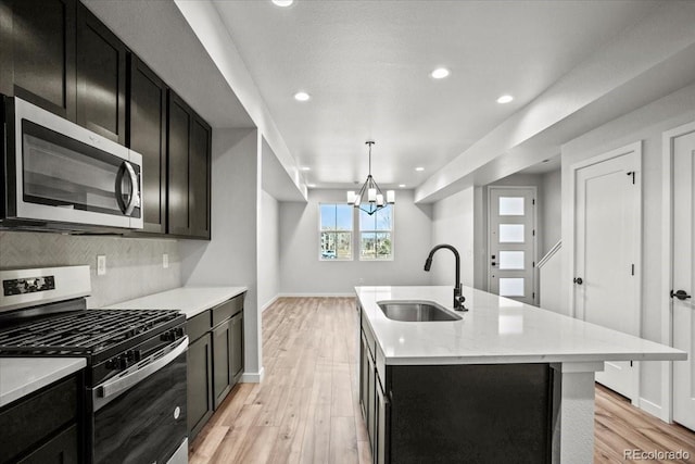 kitchen with backsplash, stainless steel appliances, dark cabinetry, and a sink
