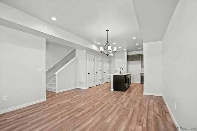 kitchen featuring open floor plan, an island with sink, light wood-style flooring, an inviting chandelier, and a sink