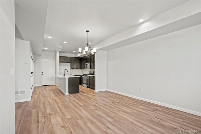 kitchen featuring light wood finished floors, open floor plan, appliances with stainless steel finishes, a notable chandelier, and a sink