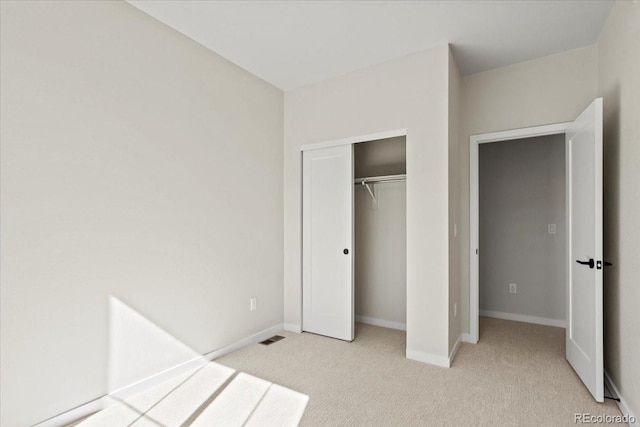 unfurnished bedroom featuring visible vents, light colored carpet, baseboards, and a closet
