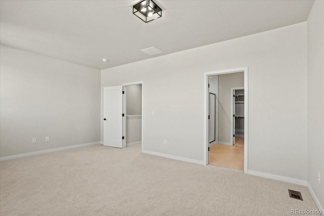 unfurnished bedroom featuring visible vents, a closet, baseboards, light colored carpet, and a spacious closet