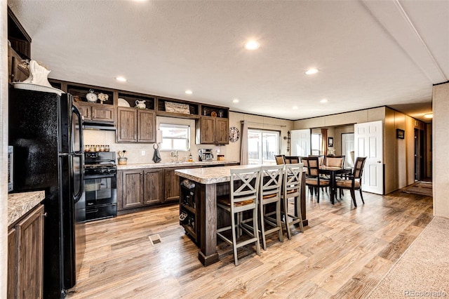 kitchen featuring black appliances, light countertops, light wood-type flooring, a kitchen breakfast bar, and a kitchen island
