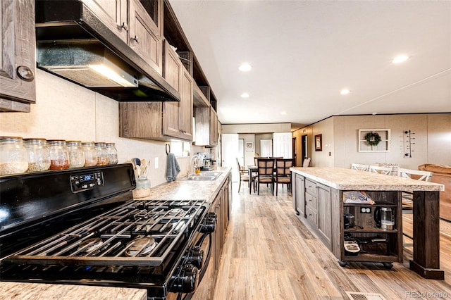 kitchen featuring gas stove, under cabinet range hood, a sink, light wood-style flooring, and light countertops
