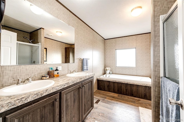 full bathroom with a stall shower, wood finished floors, crown molding, double vanity, and a garden tub