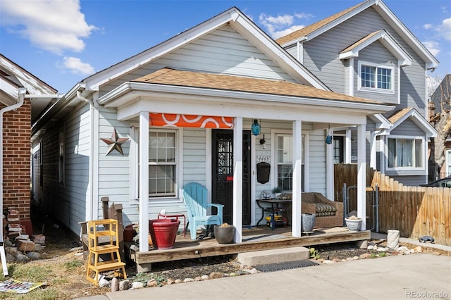 view of front of property featuring covered porch, roof with shingles, and fence