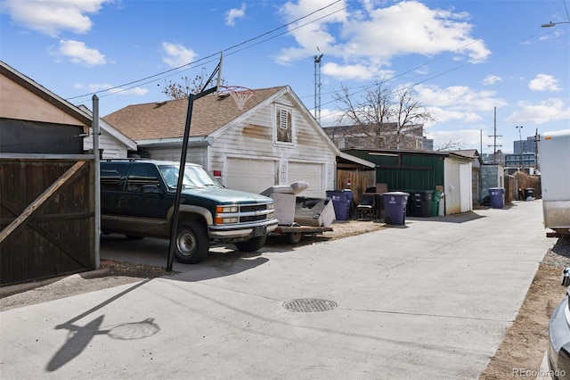 view of property exterior featuring an outdoor structure, fence, a detached garage, and a shingled roof