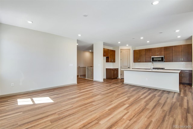 24593 E 34th Ave, Aurora, CO 80019 - kitchen featuring stainless steel microwave, light wood-style floors, recessed lighting, light countertops, and an island with sink
