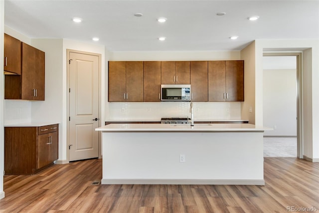 24593 E 34th Ave, Aurora, CO 80019 - kitchen with stainless steel microwave, light countertops, light wood-style flooring, a kitchen island with sink, and recessed lighting