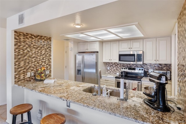 kitchen featuring a breakfast bar area, appliances with stainless steel finishes, white cabinets, decorative backsplash, and kitchen peninsula