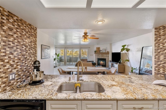 kitchen with tasteful backsplash, a tile fireplace, light stone counters, open floor plan, and a sink