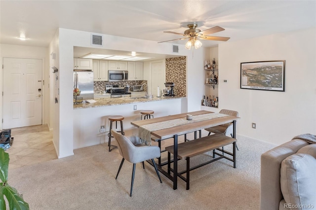 dining area with light carpet, ceiling fan, light tile patterned flooring, and visible vents