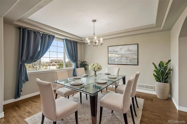 dining space with wood finished floors, visible vents, an inviting chandelier, and a raised ceiling