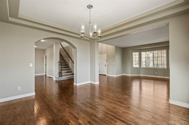 spare room featuring arched walkways, baseboards, an inviting chandelier, and wood finished floors