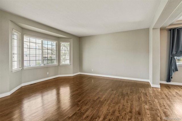 unfurnished room featuring visible vents, baseboards, and dark wood finished floors