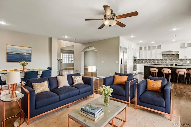 living room with baseboards, arched walkways, a ceiling fan, recessed lighting, and light wood finished floors