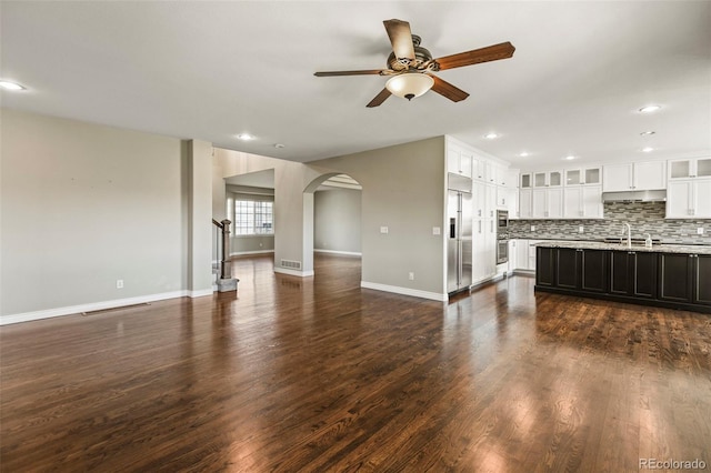 unfurnished living room with baseboards, recessed lighting, dark wood-type flooring, ceiling fan, and arched walkways