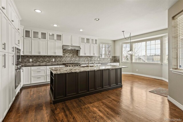 kitchen featuring white cabinets, under cabinet range hood, baseboards, and decorative backsplash