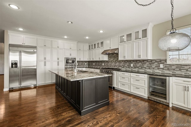 kitchen featuring white cabinets, built in appliances, under cabinet range hood, backsplash, and beverage cooler