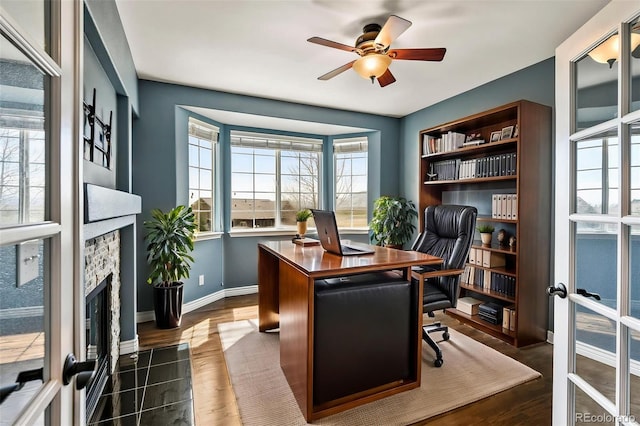 office featuring a fireplace, ceiling fan, baseboards, and dark wood-style floors