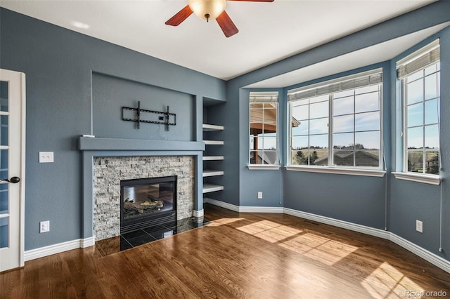 unfurnished living room featuring ceiling fan, wood finished floors, baseboards, and built in shelves