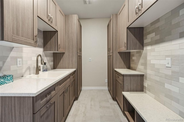 kitchen with light stone counters, a sink, backsplash, and baseboards