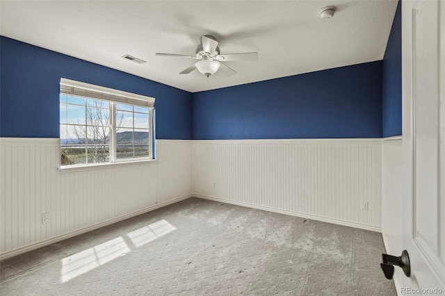 carpeted empty room featuring ceiling fan, wainscoting, and visible vents