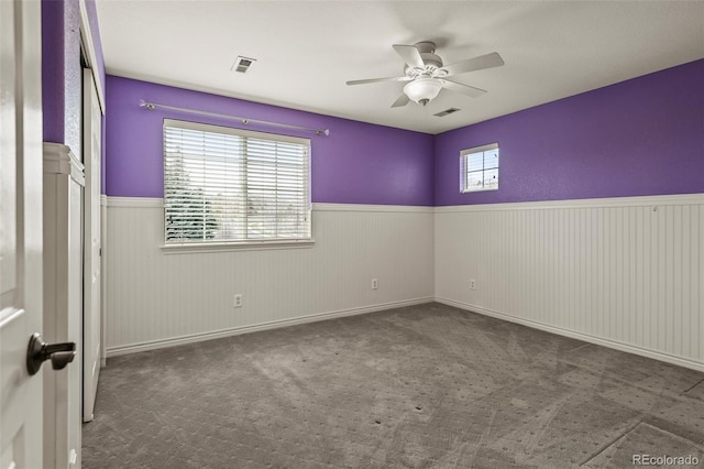 carpeted empty room featuring visible vents, a wainscoted wall, and ceiling fan