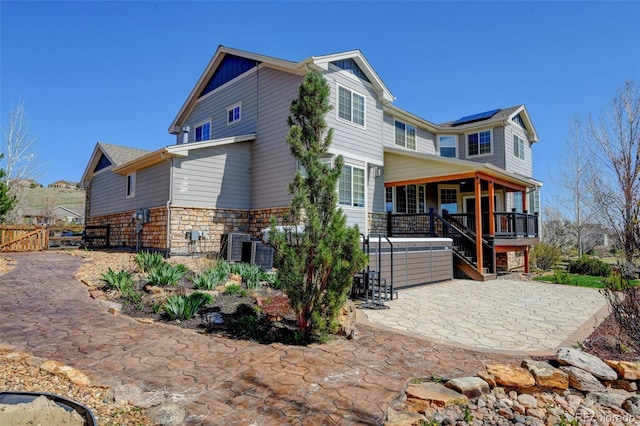 rear view of house with board and batten siding, a patio, fence, stone siding, and solar panels