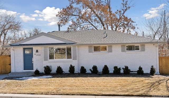 view of front of property featuring roof with shingles, fence, a front lawn, and brick siding