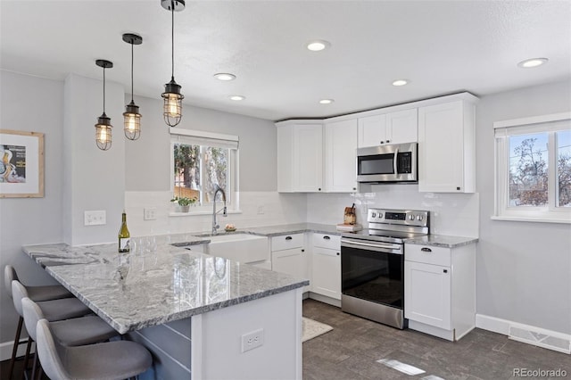 kitchen featuring stainless steel appliances, visible vents, a sink, light stone countertops, and a peninsula