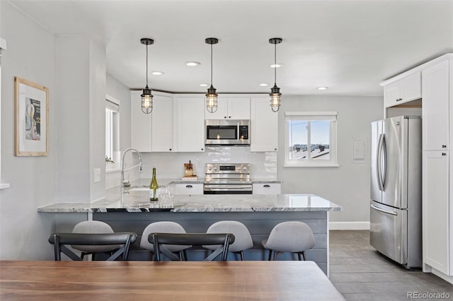 kitchen featuring light stone counters, stainless steel appliances, backsplash, white cabinetry, and a peninsula