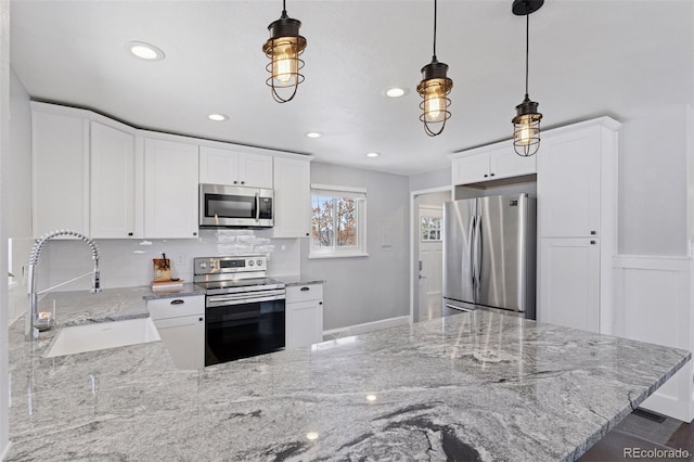 kitchen featuring a peninsula, a sink, appliances with stainless steel finishes, light stone countertops, and decorative light fixtures