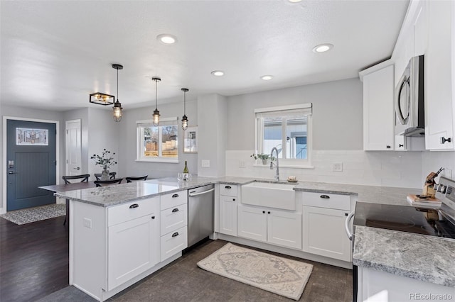 kitchen featuring stainless steel appliances, a healthy amount of sunlight, white cabinets, a sink, and a peninsula