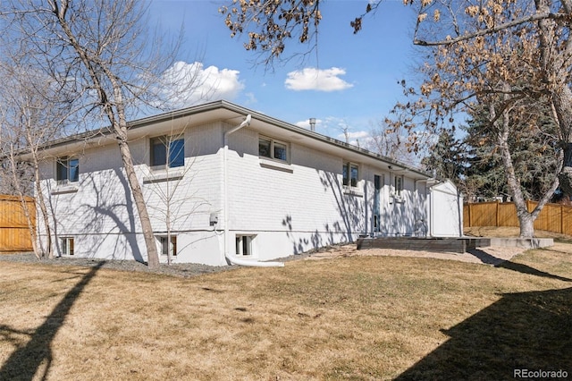 back of house featuring fence, a lawn, and brick siding