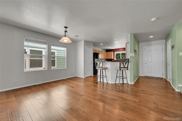 18947 E 57th Pl, Denver, CO 80249 - kitchen featuring freestanding refrigerator, a peninsula, a textured ceiling, wood finished floors, and a kitchen breakfast bar