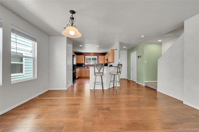18947 E 57th Pl, Denver, CO 80249 - kitchen with light wood-style flooring, a breakfast bar area, dark countertops, a textured ceiling, and recessed lighting