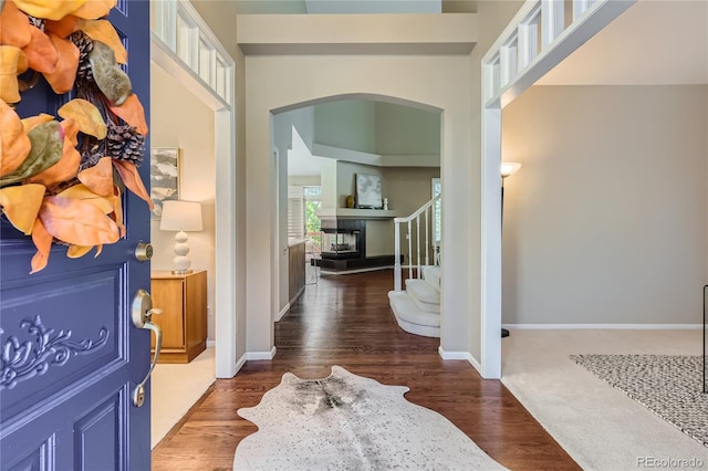 foyer entrance featuring dark wood-type flooring, a multi sided fireplace, and a high ceiling