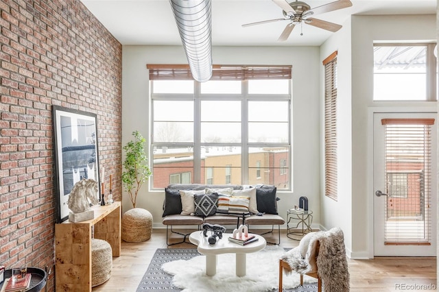 living area with light hardwood / wood-style floors, ceiling fan, a healthy amount of sunlight, and brick wall