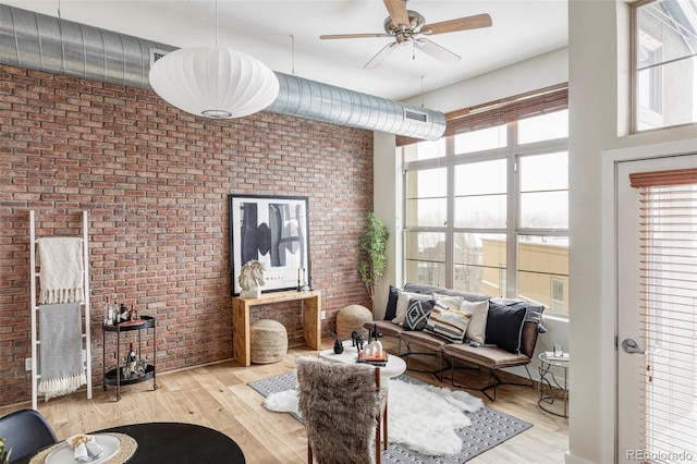 interior space featuring ceiling fan, light wood-type flooring, a high ceiling, and brick wall