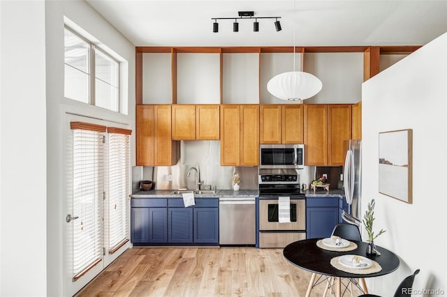 kitchen with decorative backsplash, appliances with stainless steel finishes, sink, light hardwood / wood-style flooring, and hanging light fixtures