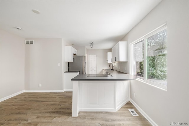 kitchen featuring kitchen peninsula, stainless steel fridge, sink, light hardwood / wood-style floors, and white cabinetry