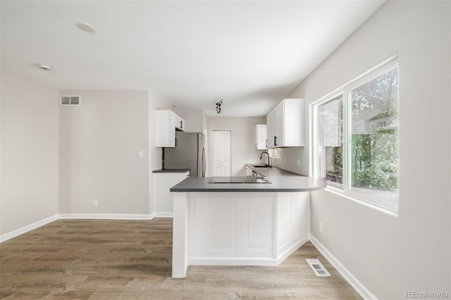 kitchen with light wood finished floors, white cabinets, freestanding refrigerator, and visible vents