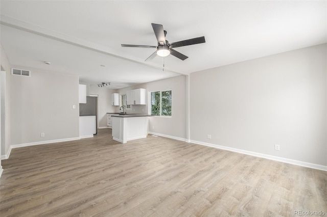 unfurnished living room featuring visible vents, baseboards, a sink, ceiling fan, and light wood-style floors