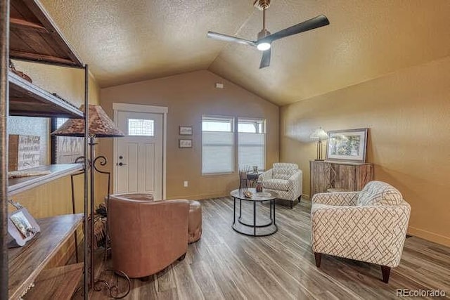 living area featuring ceiling fan, hardwood / wood-style flooring, vaulted ceiling, and a textured ceiling