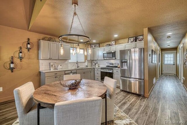 kitchen featuring sink, tasteful backsplash, decorative light fixtures, appliances with stainless steel finishes, and hardwood / wood-style floors