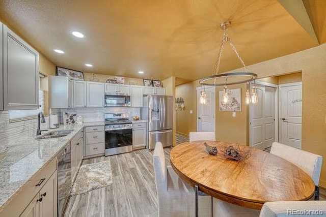 kitchen with sink, appliances with stainless steel finishes, hanging light fixtures, tasteful backsplash, and light wood-type flooring