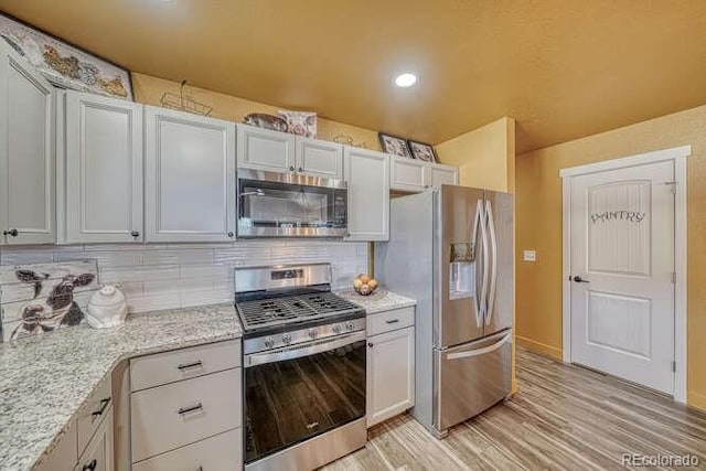 kitchen featuring tasteful backsplash, light hardwood / wood-style flooring, stainless steel appliances, light stone countertops, and white cabinets