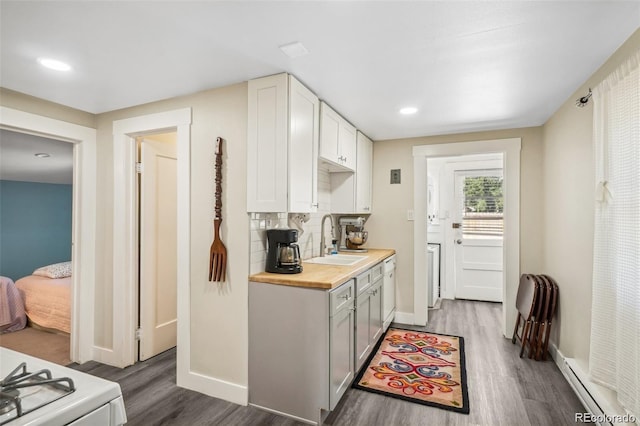 kitchen featuring a sink, wood finished floors, wood counters, baseboard heating, and backsplash