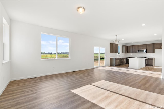 unfurnished living room with a chandelier, sink, and light hardwood / wood-style flooring